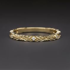 a yellow gold wedding ring with diamonds on the sides and leaves in the middle, against a black background