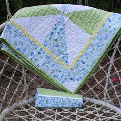 a blue and green quilt sitting on top of a white chair next to a pillow