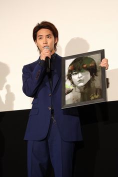 a man in a blue suit holds up a framed photo while standing next to a microphone