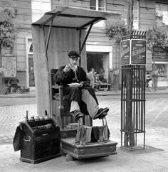 a man sitting on top of a pile of luggage next to a street sign and telephone booth