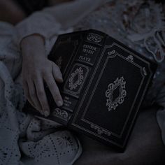 a person holding an old book in their hand while laying on a bed at night