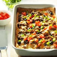 a casserole dish with meat and vegetables in it next to a bowl of tomatoes