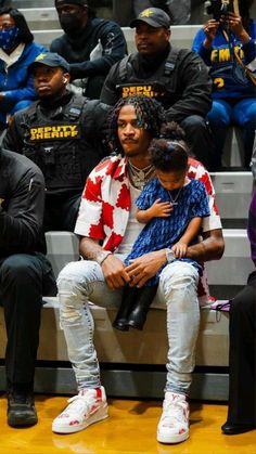 a man holding a child sitting on top of a bench in front of other people