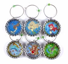 six bottle caps with mermaids on them are hanging from the side of each other