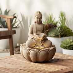 a buddha statue sitting on top of a wooden table next to potted greenery