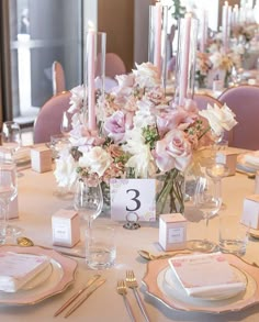 the table is set with pink and white flowers in vases, candles, and place cards