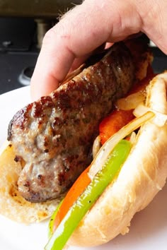 a sausage sandwich on a bun with peppers and onions is being held by a hand