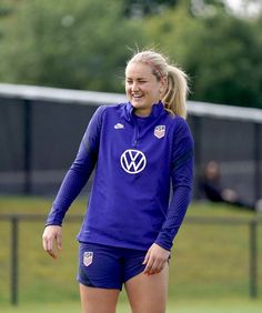 a woman in blue soccer uniform standing on the field with her hands behind her back