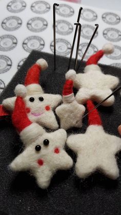 needled christmas ornaments are sitting on top of a black piece of fabric with pins in the shape of santa's hats