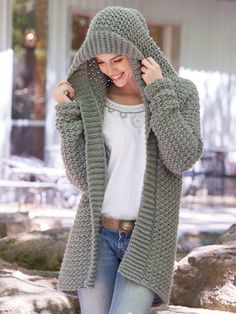 a woman is wearing a green knitted cardigan and smiling at the camera while standing in front of some rocks