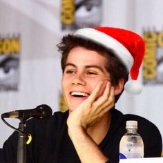 a young man wearing a santa hat sitting at a table in front of a microphone