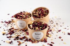 three cups filled with dried flowers on top of a white tablecloth covered in confetti