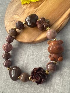 a necklace with flowers and beads on it next to a wooden plate holding a yellow flower