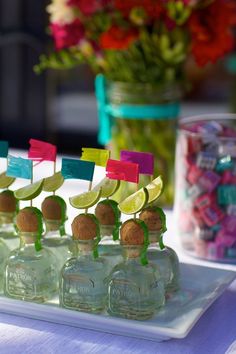 several small bottles with lemon slices in them on a tray next to flowers and candy