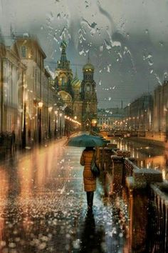 a person holding an umbrella in the rain on a city street with buildings and lights