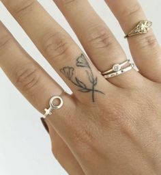 a woman's hand with three rings on it and a flower tattoo on the middle finger