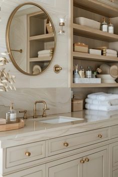 a white bathroom with gold accents and marble counter tops, along with towels on the shelves