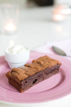 a piece of cake sitting on top of a pink plate next to a bowl of whipped cream