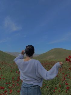 a woman standing in a field with red flowers