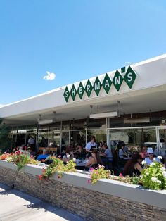 people sitting at tables in front of a restaurant with green and white awnings