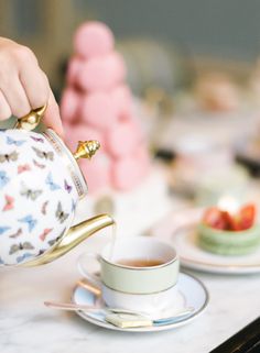 a person pouring tea into a cup on top of a white plate with gold trim