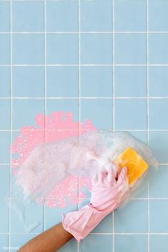 a person's hand holding a sponge over a blue tiled wall