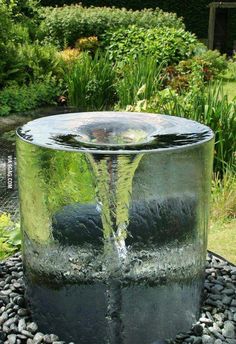 a water fountain in the middle of a garden with rocks and gravel around it, surrounded by greenery