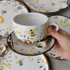 a hand holding a coffee cup and saucer with yellow flowers on it, surrounded by plates