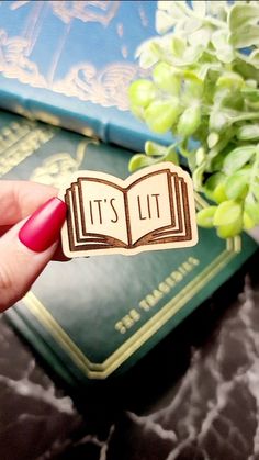 a hand holding a book shaped magnet that says it's lit