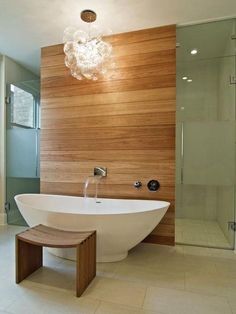 a large white bath tub sitting next to a wooden wall in a bathroom under a chandelier