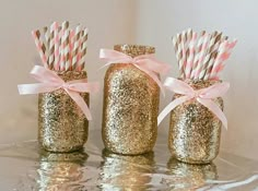 three gold glitter mason jars with pink and white striped straws