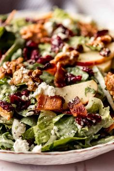 a salad with apples, cranberries and bacon on it in a white bowl