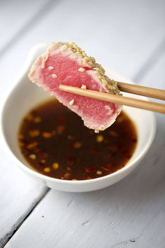 chopsticks sticking out of a bowl filled with soup and sauce on a white table