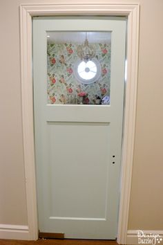 a white door with a clock on the side and wallpaper behind it in a room