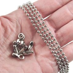 a hand holding a silver chain with a small frog charm on it's end