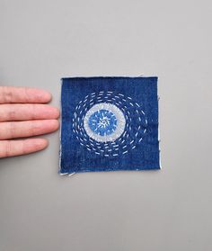 a hand is holding a piece of fabric with a blue and white design on it