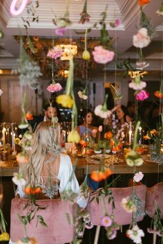 a woman sitting at a bar with flowers hanging from the ceiling and candles in front of her