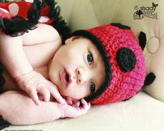 a baby wearing a red and black crocheted hat laying on top of a couch