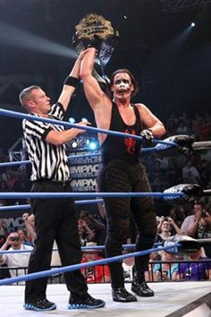 two men standing on top of a wrestling ring holding up a metal object in the air