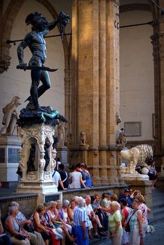 a group of people standing around a statue in a building with columns and arches on both sides