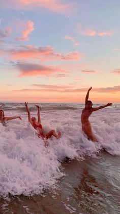 three people are in the water and one is falling off his surfboard while another person holds their arms up