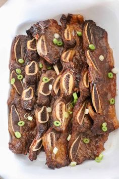 there is some meat on a white plate with green onions and garnishes