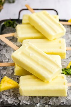 four popsicles on top of ice with pineapples and mint leaves in the background