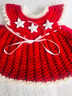 a crocheted dress with white flowers on the front and red, ruffled bottom