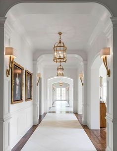 an empty hallway with white walls and wood flooring, framed pictures on the wall