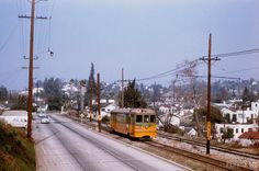 a yellow train traveling down tracks next to a street filled with houses and power lines