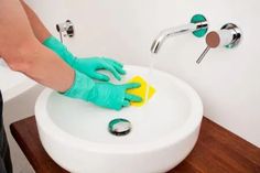 a person in blue gloves cleaning a white sink with a yellow sponge and green rag