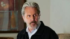 an older man with grey hair wearing a black jacket and white shirt in a living room