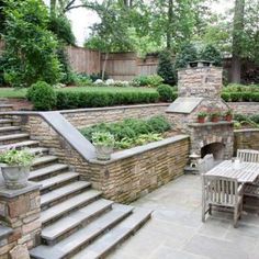 an outdoor patio with stone walls and steps leading up to the fire place, surrounded by greenery