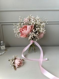 a bouquet of pink roses and baby's breath on a white table with a ribbon